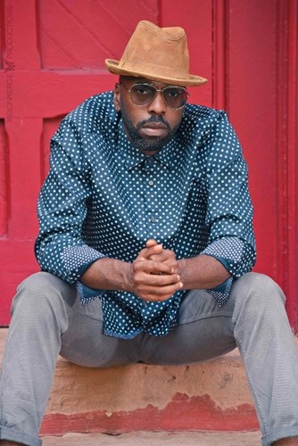 Dr. Davarian L. Baldwin sits on a concrete step outside of a red door.